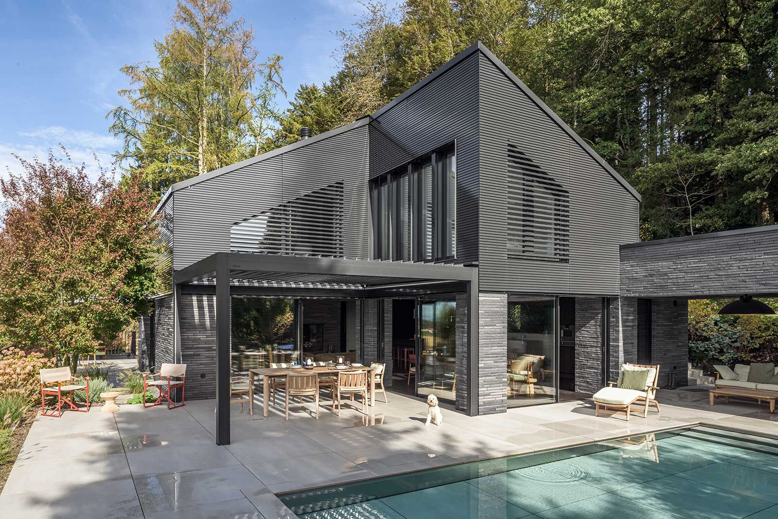 Handgefertigte Ziegel ummanteln das Erdgeschoss. ­Horizontal ­angebrachte Metalllamellen im Obergeschoss ­korrespondieren  mit den ­Erdtönen der Backsteine. Der Pool von Flusspool lässt sich per Knopfdruck auf das Niveau der Terrasse anheben und vergrössert so den Outdoorbereich.