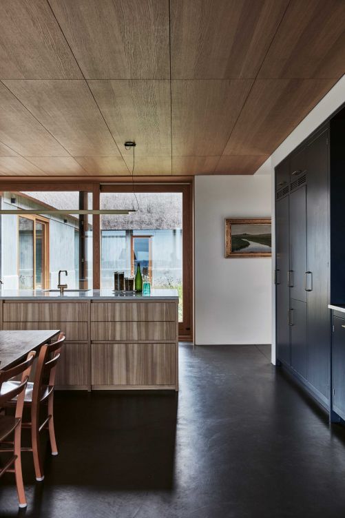 Das Konzept der Landhausküche erhielt ein Upgrade in einem minimalistischen, hellen Look mit Betonböden, Schiebetüren zum Innenhof und einer langgestreckten Kochinsel aus Eschenholz. Küche: Kvänum; Leuchte: Louis Poulsen.