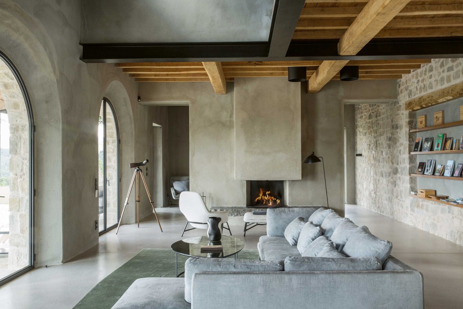 Im Inneren des Hauses trifft Kalkzementputz auf Naturstein und Kastanienholz auf schwarz gestrichenen Stahl. Die Interior Designerin Stephanie Thatenhorst kombinierte im Wohnraum ein Sofa von Verzelloni mit einem Couchtisch von Ochre. Lässig dazu der Lounger von Minotti und die Stehleuchte von Serge Mouille.