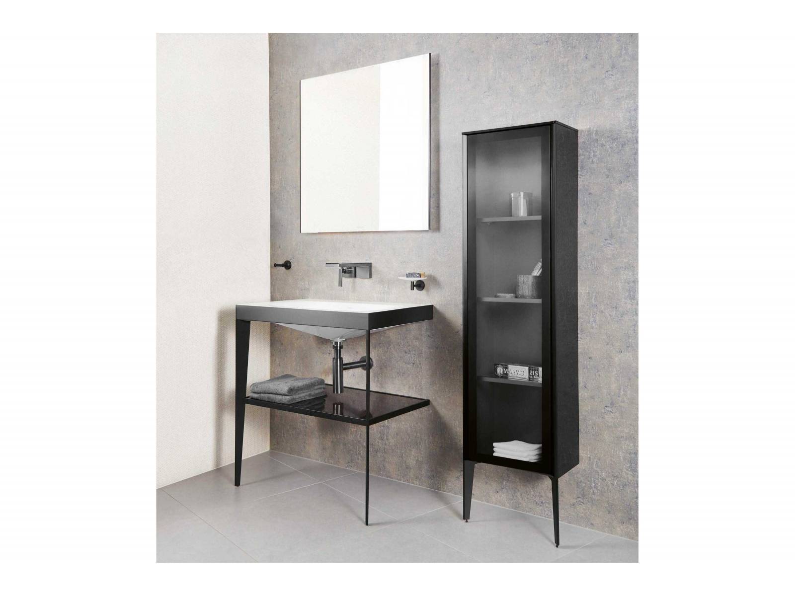 Das elegante Schwarz der Badmöbel ist in diesem Fall bloss einer der Schlankmacher. Regal und Schrank besitzen jeweils nur zwei Beine und sind rückseitig an der Wand befestigt. Das spart Platz, wenn er rar ist und wirkt mit kraftvollen Linien ebenso im geräumigen Bad. Der grosszügige Lichtspiegel und das breite Lavabo erleichtern das Handling. Sabag.