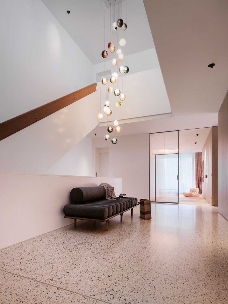 Eingangsbereich und Treppenhaus öffnen sich weit und beeindrucken mit einer überhöhten Decke. Die Holzflächen verleihen dem Raum eine sanfte ­Eleganz, während Glasschiebetüren den Blick in angrenzende Räume lenken. Eine Leuchte von Bocci setzt kunstvolle ­Akzente. Das Treppengeländer veredelte die Architektin durch einen Alcantara-Aufsatz. Im Zentrum des Raumes: das Daybed «Five to Nine» von Studiopepe für Tacchini.
