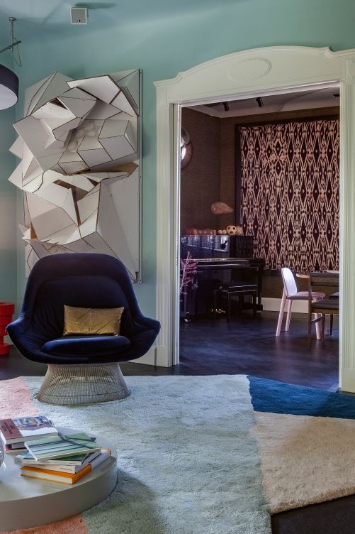 Das Wohnzimmer ist in verschiedenen Blau- und Lilatönen gehalten. Von hier geht der Blick ins Esszimmer. Eyecatcher im Raum ist der blaue Sessel «Easy Chair» von Warren Plattner für Knoll International, der auf einem Teppich von Oliver Treutlein steht. Das 3D-Kunstwerk an der Wand stammt vom deutschen Künstler Florian Baudrexel, dessen Skulpturen plastische Elemente aus Gips, Pappe, Styropor und anderen alltäglichen Stoffen sind.